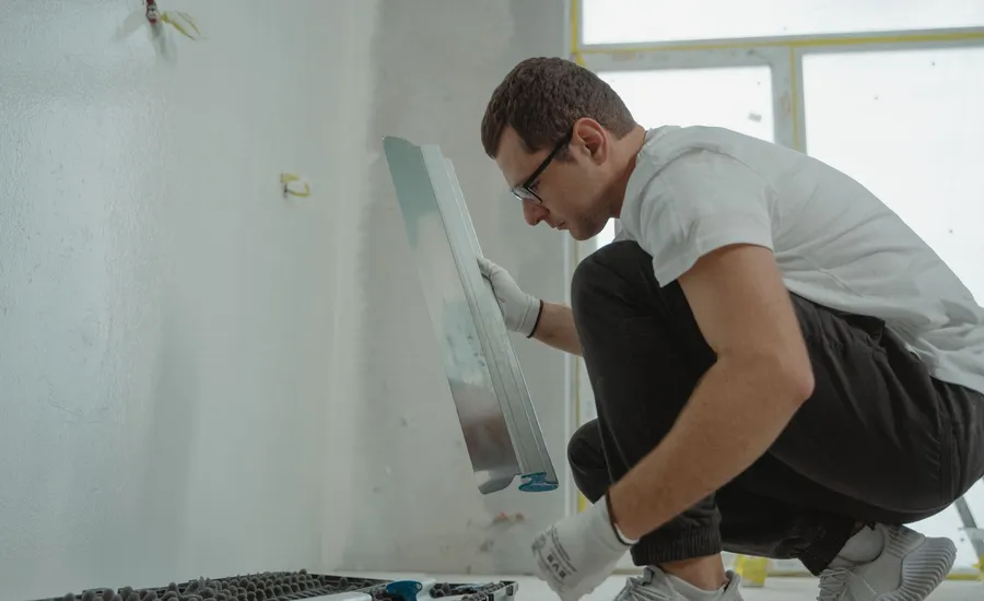 A tradesperson kneeling to apply plaster to an interior wall during renovation work
